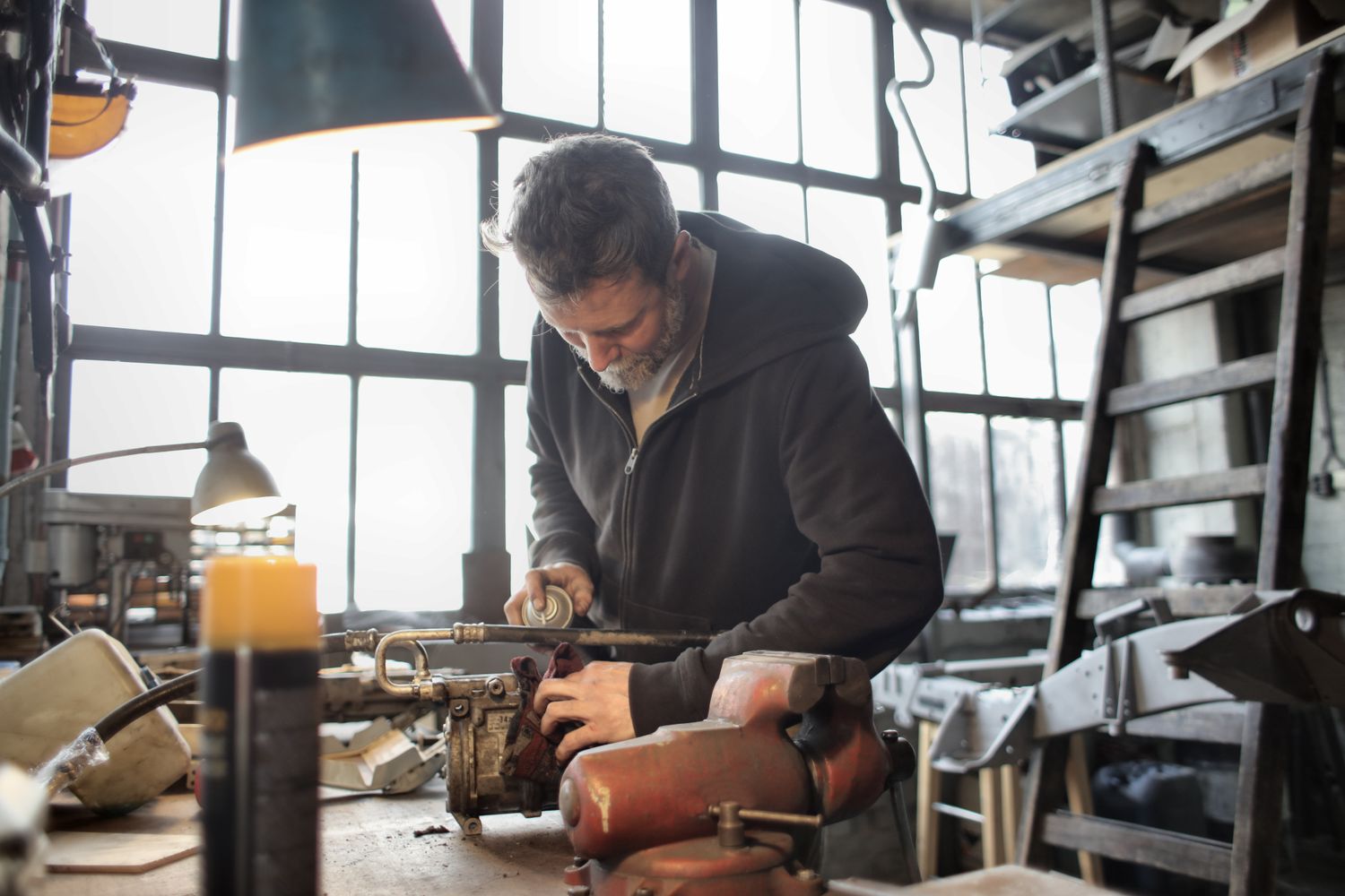 Male craftsman in casual outfit fixing old rusty detail in workshop and using aerosol paint while standing at workbench and working