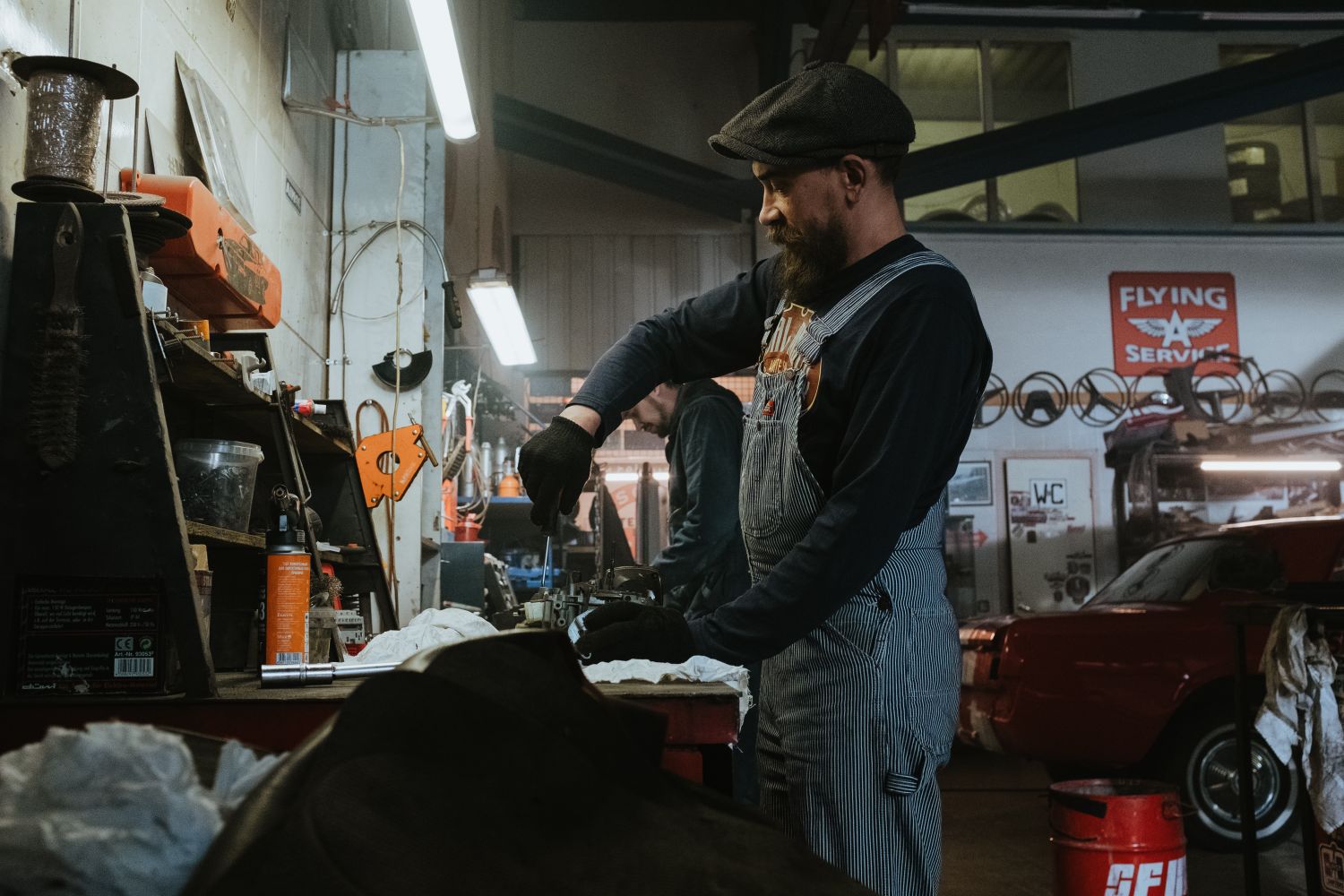 Mechanic performing repairs in a vintage garage setting, using tools and machinery.
