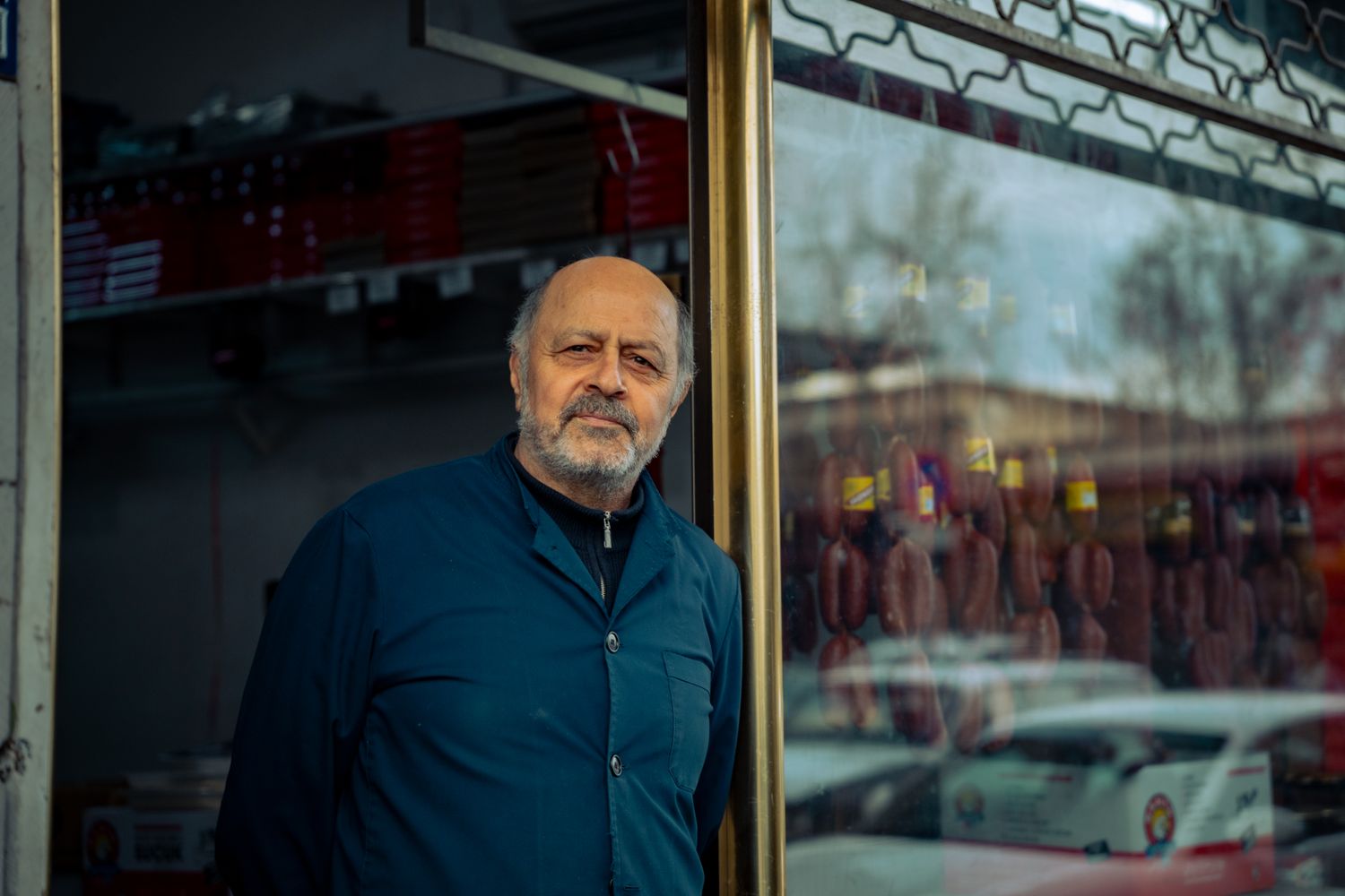Elderly butcher standing proudly outside his traditional meat shop.