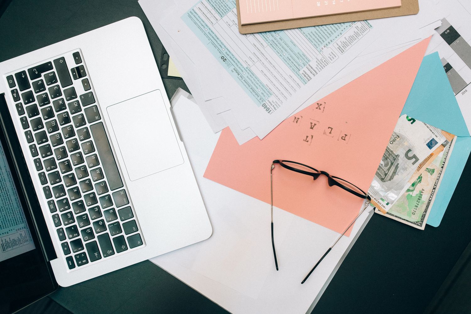 A tidy workspace featuring a laptop, documents, and eyeglasses for productivity.