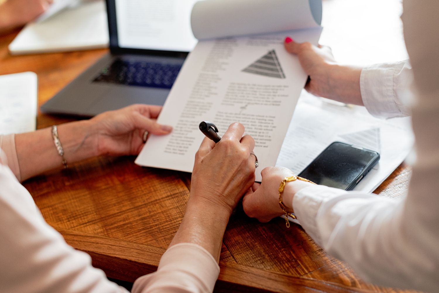 Two women reviewing documents at a table, engaging in a work discussion.