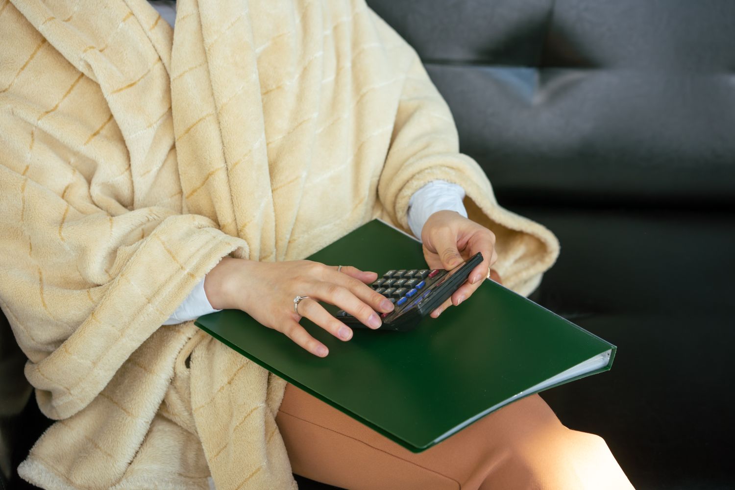 Close-up of hands using a calculator on a file folder, wearing a cozy robe.