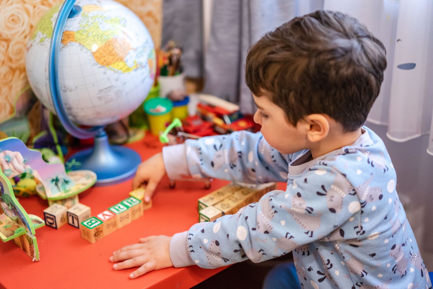 A young boy engages with alphabet blocks and a globe, learning through play indoors.
